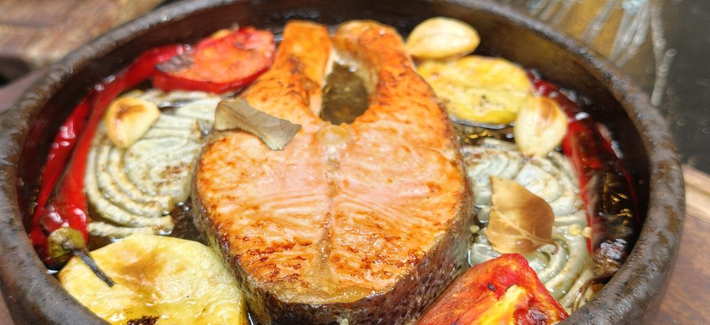 Premium Norwegian Butter Salmon cooked in a traditional stone oven with butter, roasted potatoes, garlic, tomatoes and peppers at Nasreddin Restaurant in Antalya